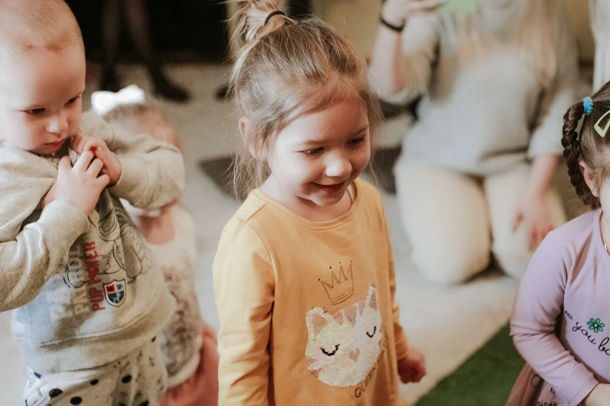 Eltern und Kinder betreten gemeinsam eine moderne Kita-Einrichtung, Betreuungspersonal empfängt die Familien freundlich