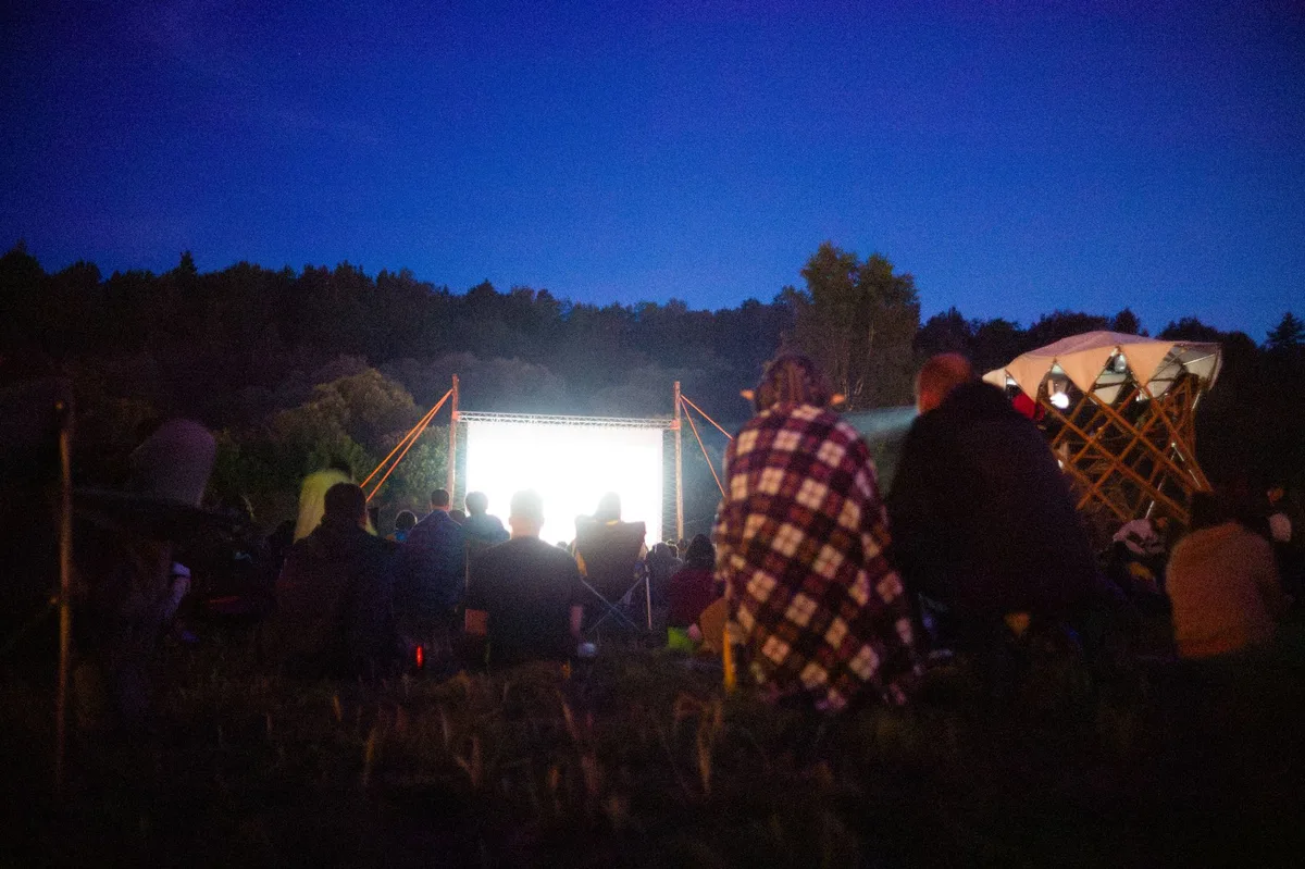 Zuschauer sitzen auf Decken beim Freiluftkino und schauen auf die Leinwand