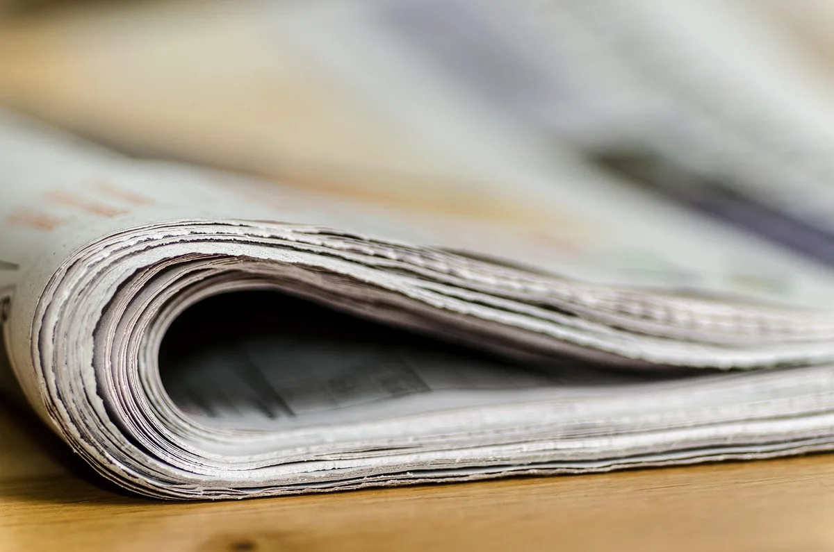 Kleiner Cafétisch am Fenster mit Kaffee, Stück Käsekuchen und Zeitung