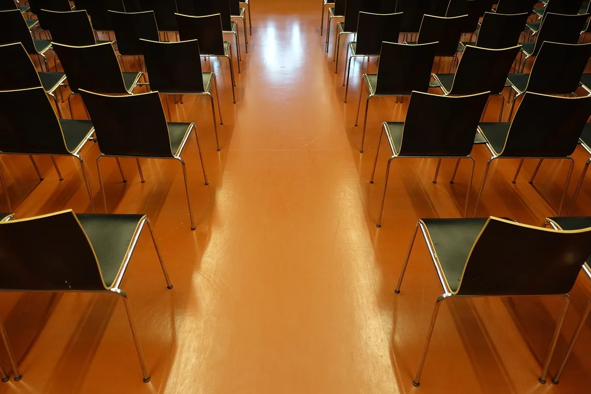 Anonyme Konferenzlobby mit Silhouetten, leeren Registrierungstischen und gestapelten Stühlen