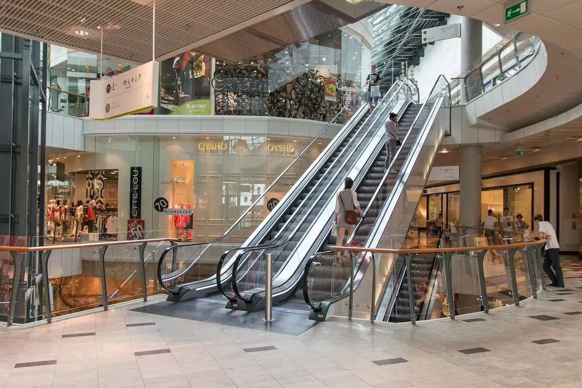 Blick in ein Einkaufszentrum mit Gerüst, Rolltreppen und anonymen Silhouetten